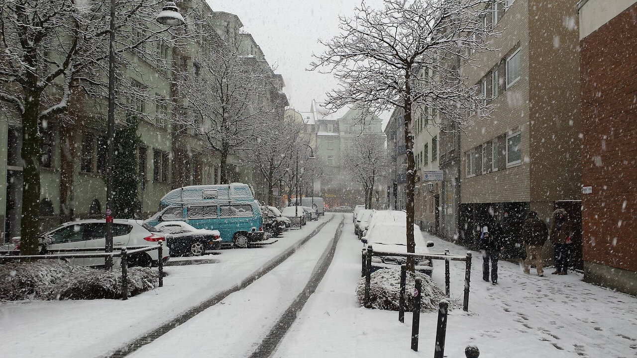 A commercial street covered in snow with a trail left by the tires of passing cars.